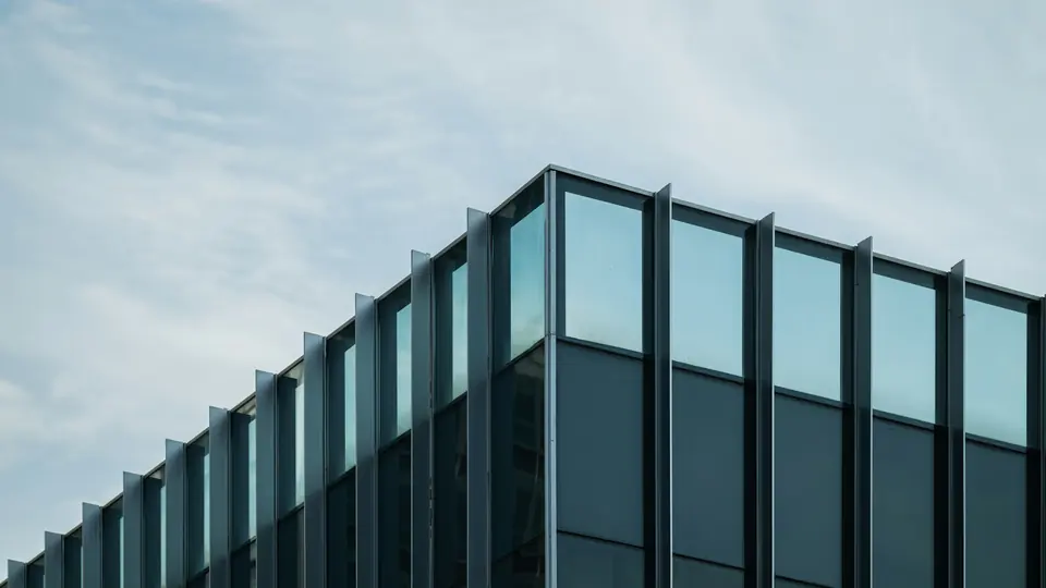 Kontorshus med glasfasad i svarta profiler mot en ljus himmel